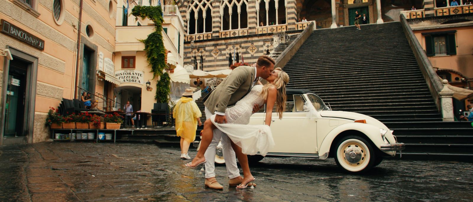 Chelsea and Nicholas kissing beside a vintage car in the piazza at Amalfi