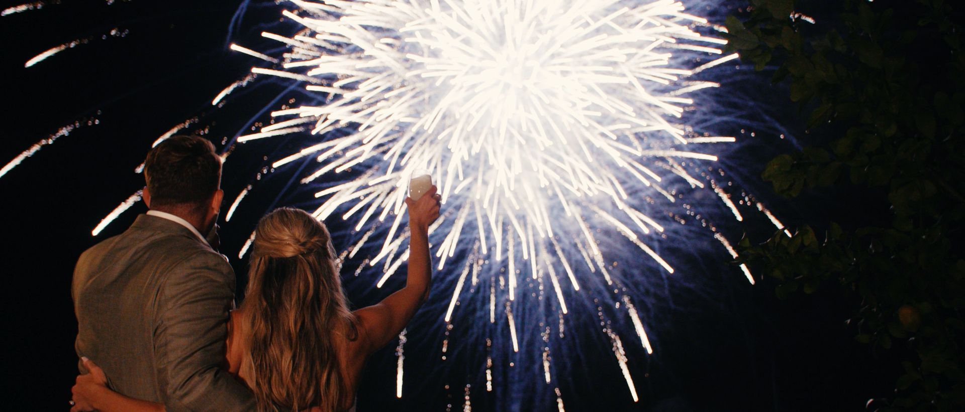 Chelsea and Nicholas raising a glass beneath fireworks