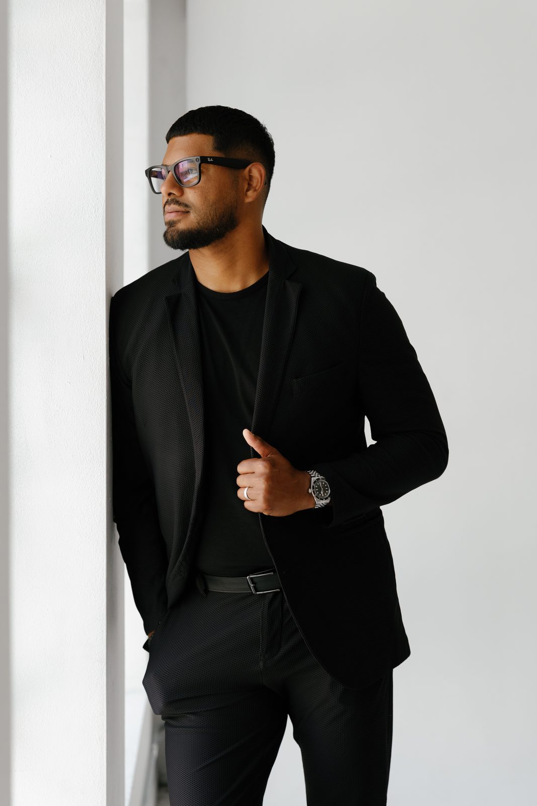 Javi in glasses and a black blazer, leaning on a wall