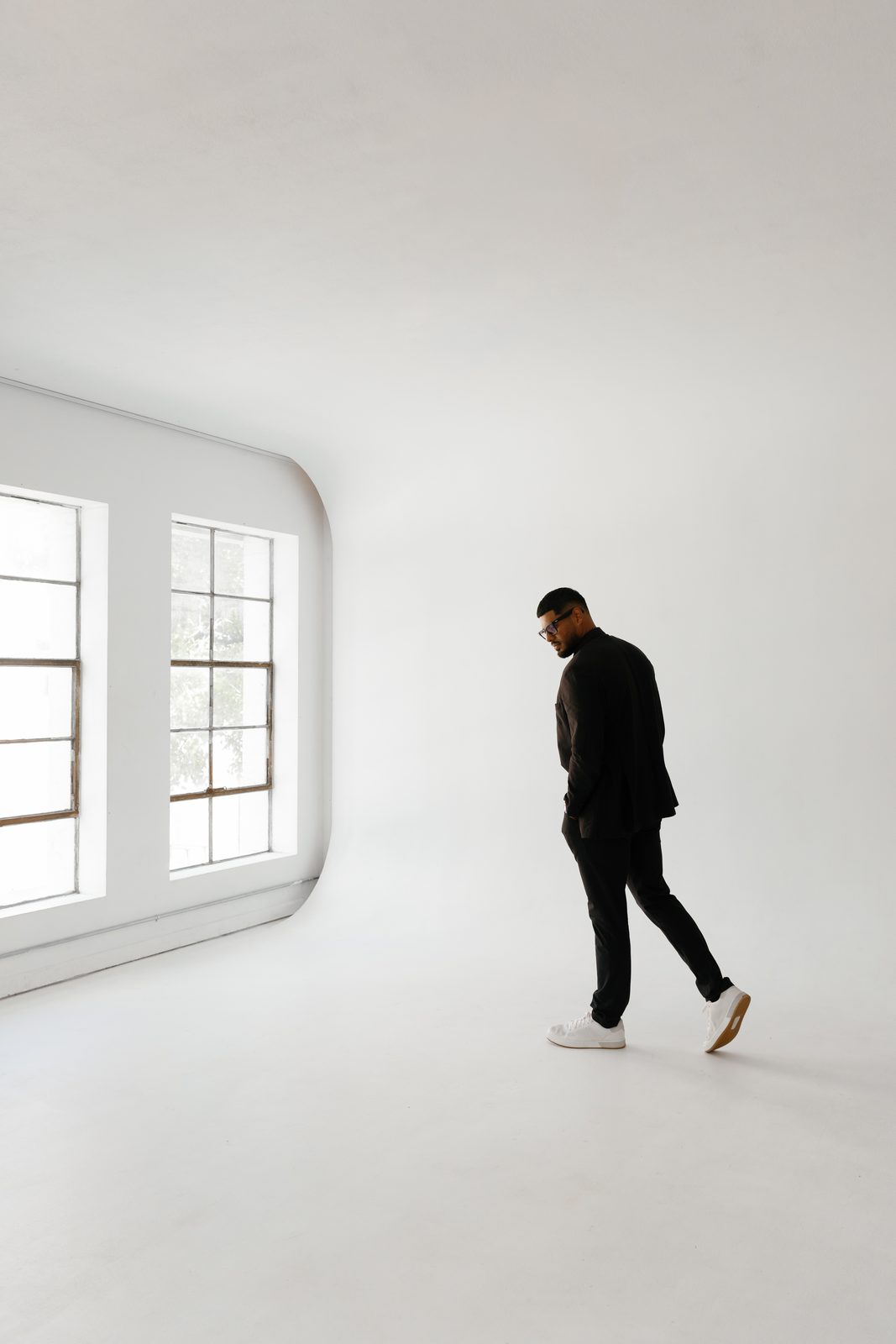 Javi walking toward tall windows in a black suit